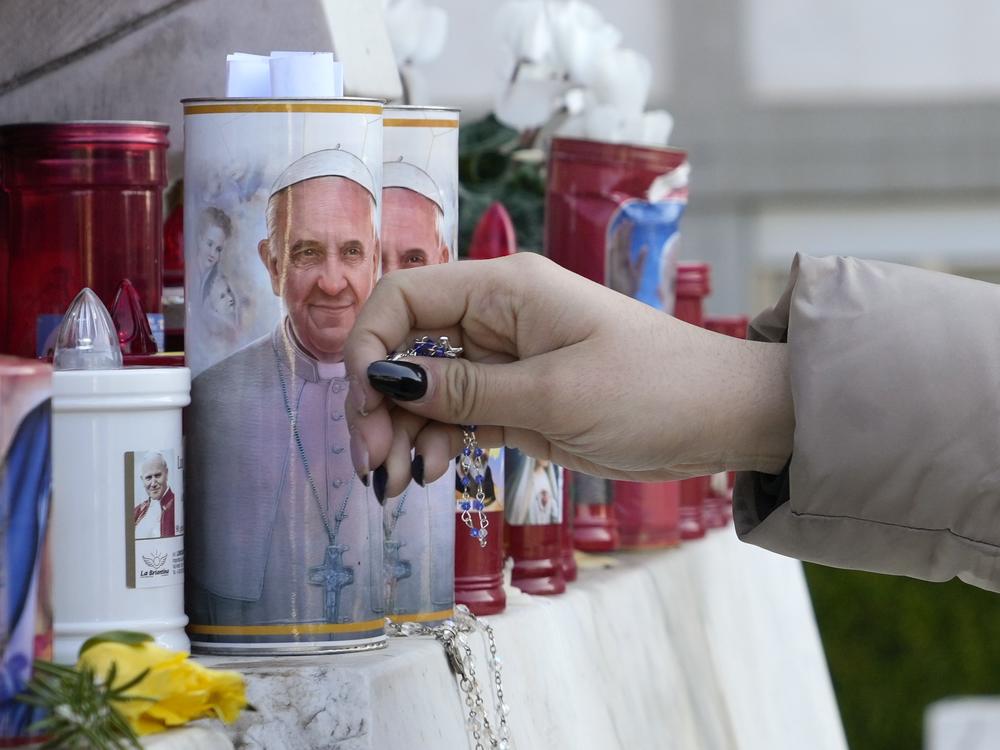 A woman lays a rosary on Saturday near candles adorned with pictures of Pope Francis outside the Agostino Gemelli Polyclinic where Pope Francis is battling pneumonia in Rome.