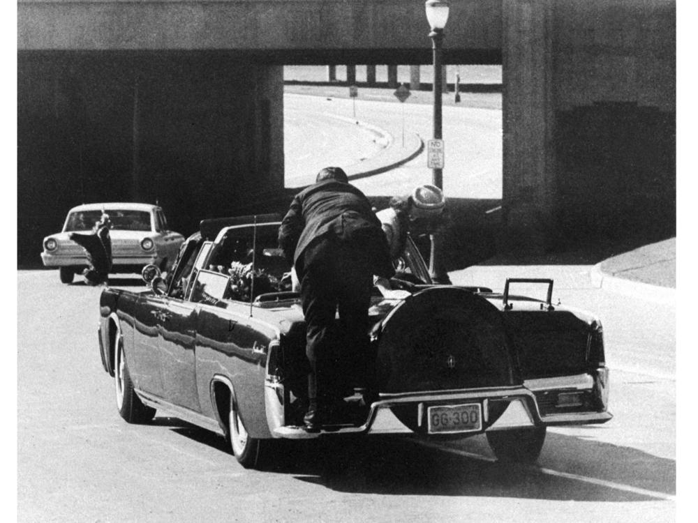 President John F. Kennedy slumps down in the back seat of the presidential limousine as it speeds along Elm Street toward the Stemmons Freeway overpass in Dallas, Texas, after being fatally shot, Nov. 22, 1963. First lady Jacqueline Kennedy leans over the president as Secret Service Agent Clint Hill pushes her back to her seat.