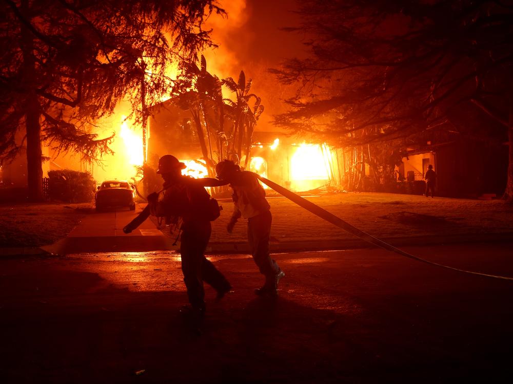Los Angeles County firefighters pull a hose in front of a burning home as the Eaton Fire moved through the area on Jan. 8 in Altadena, Calif.