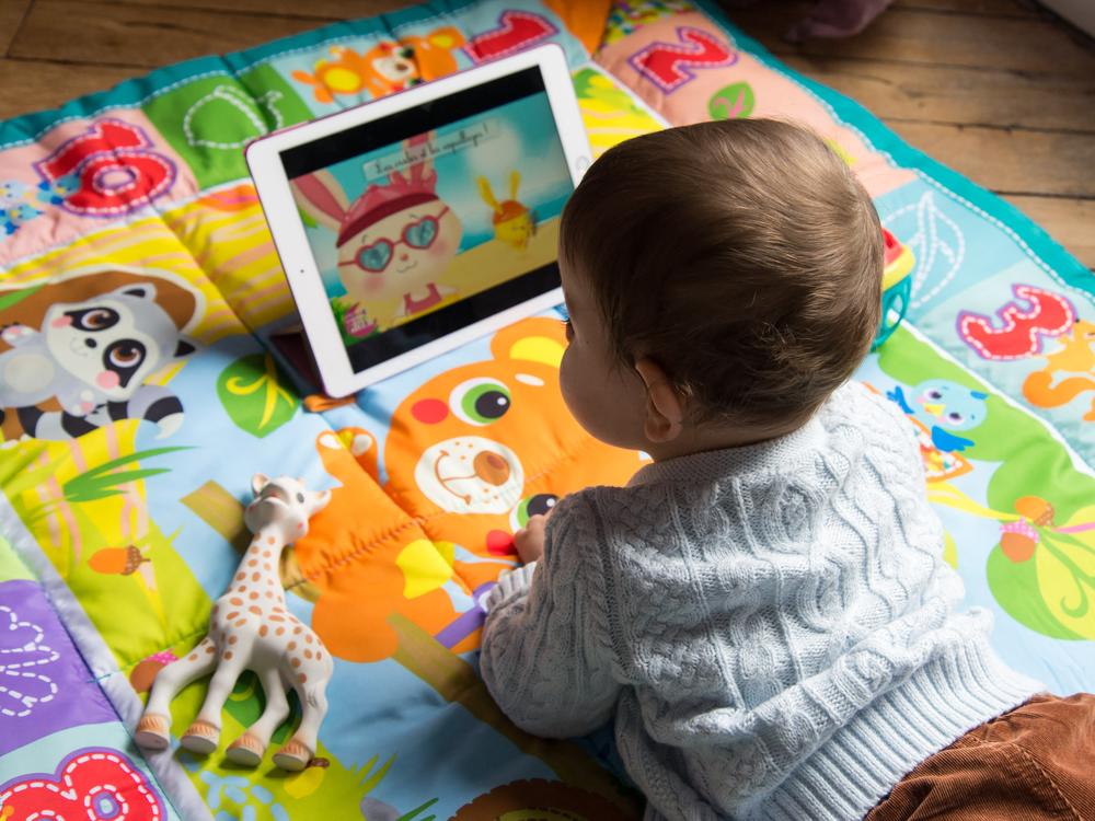 An 8-month-old baby watches a cartoon on a tablet. A survey by Common Sense Media found that 80% of parents are worried about their children spending too much time on screens.