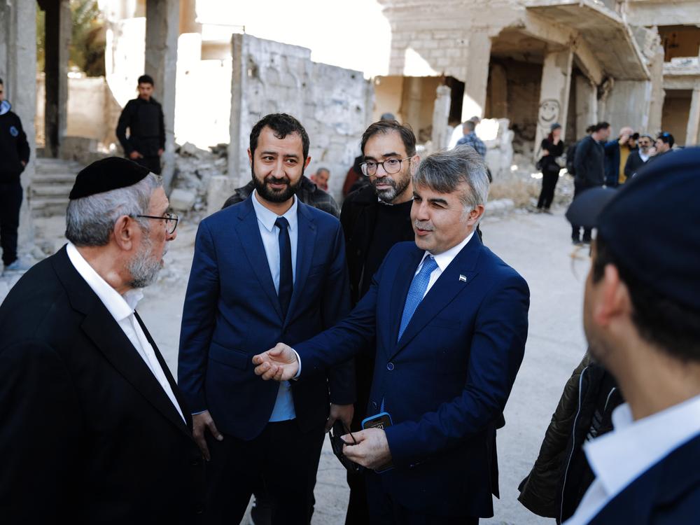 Syria's new leader sent a key advisor, Moussa al-Omar (right), to meet the delegation in a trip to Syria organized by Syrian-American activists Mouaz Moustafa (second from left). In the background is the destroyed Damascus suburb of Jobar.