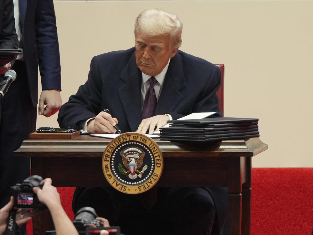 President Donald Trump signs an executive order at an indoor Presidential Inauguration parade event in Washington, Jan. 20, 2025.