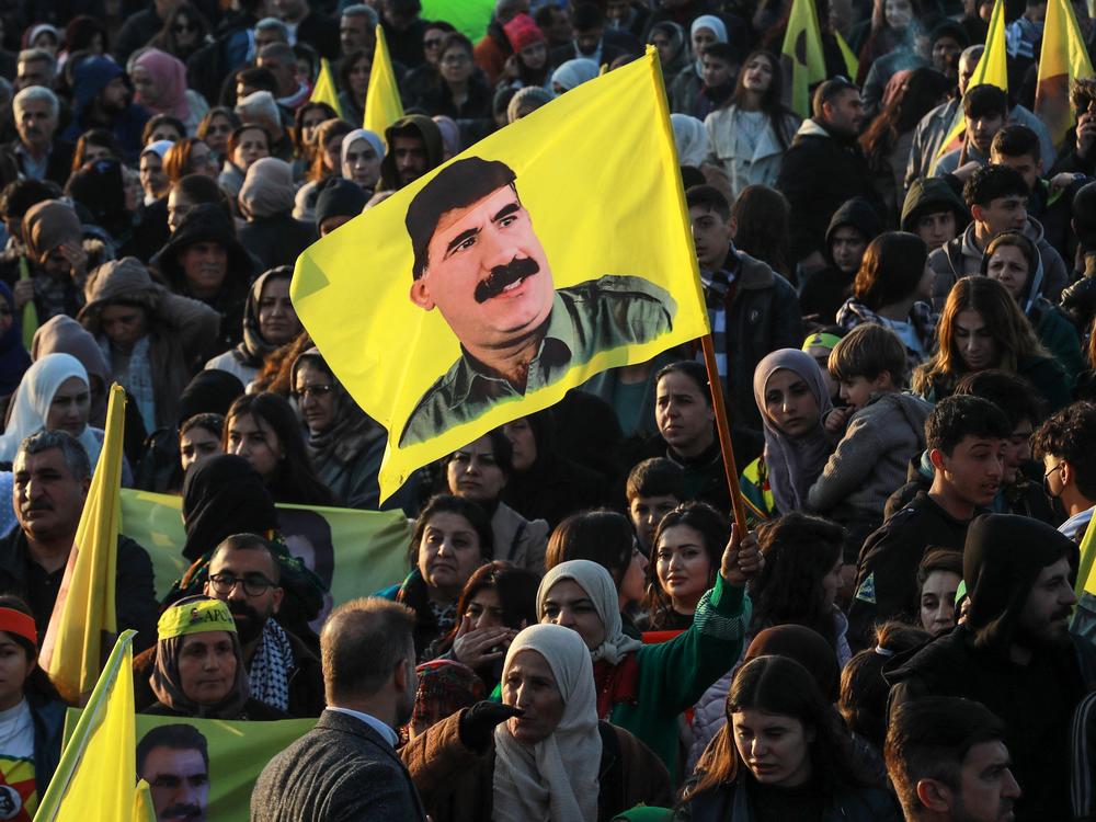 A woman waves a flag bearing a picture of the founder of the Kurdistan Workers' Party (PKK) Abdullah Ocalan, as people gather in the Kurdish-majority city of Qamishli in northeastern Syria to listen to a message from the jailed leader on Feb. 27. Ocalan called for his Kurdish militant force to disband and his fighters to lay down their arms.