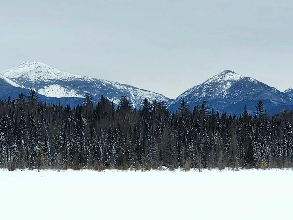 A snowshoe trek to Wolf Pond in New York's Adirondack Mountains. After breaking trail through the woods, the icy lake opens up to views of the High Peaks Wilderness.