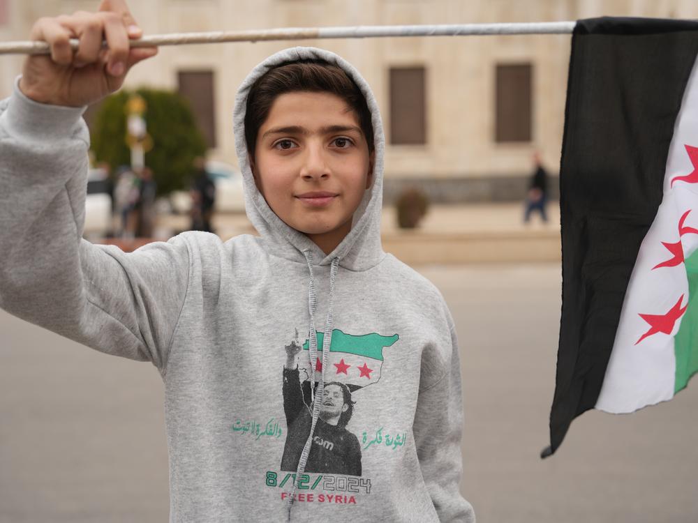 A boy in the city of Hama wears a sweater with a photo Ayman al-Masri, pictured above the date Dec. 8, 2024, to commemorate the fall of the Assad regime.