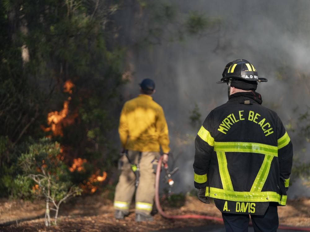 Firefighters attend to a flare-up in the Carolina Forest neighborhood on Sunday in Myrtle Beach, S.C. Multiple forest fires in the area caused evacuations along the South Carolina coast. A storm is expected to bring extreme weather and wildfire risk to various regions across the U.S. this week.