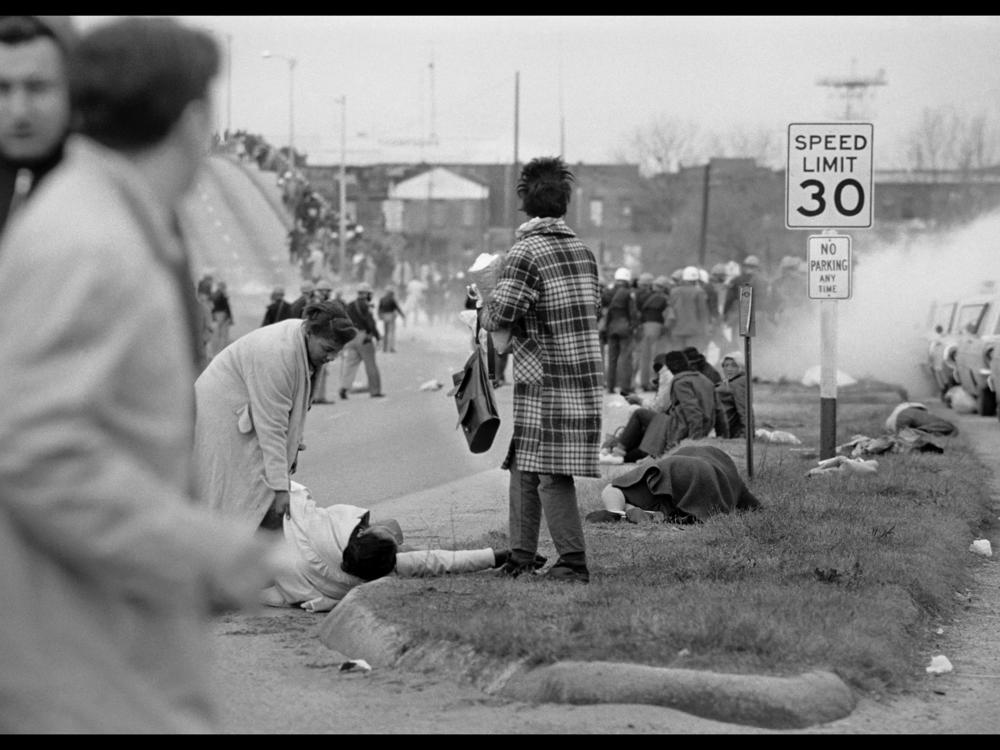 Marchers flee across the bridge as an unidentified woman assists a still-unconscious Amelia Boynton.