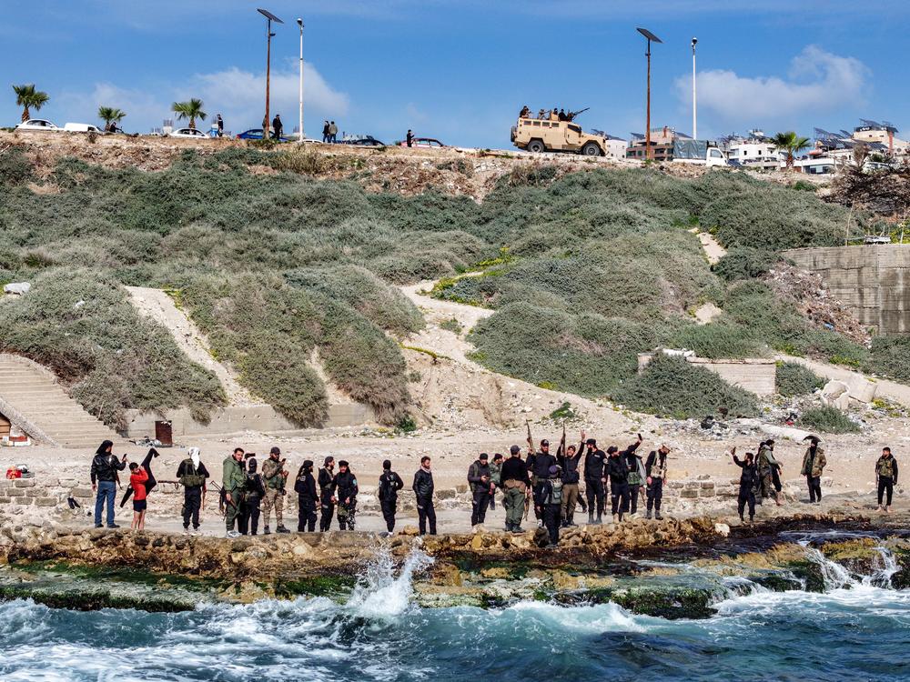 This aerial view shows members of security forces loyal to the interim Syrian government standing along a rocky beaech by Mediterranean sea coast in Syria's western city of Latakia on March 9.