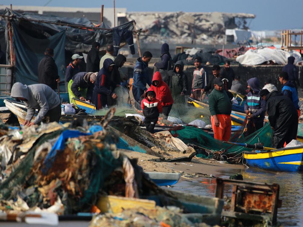Palestinians gather with fishermen at the port of Gaza City on Sunday. Israeli bombardment over more than 15 months of war between Israel and Hamas has destroyed most of the boats in the harbor, wrecking the fishermen's ability to make a living and provide food to people in Gaza.
