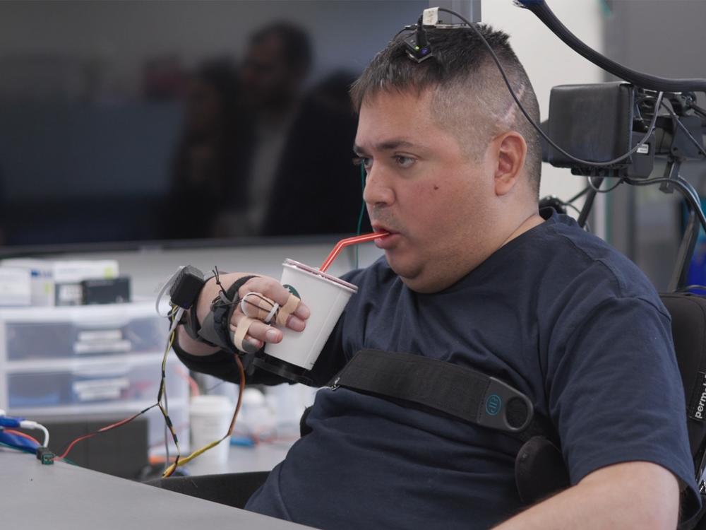 Keith Thomas, who has lived with paralysis since a diving accident in 2020, grasps, lifts and drinks from a cup on his own. Brain implants and artificial intelligence  bypass his injury and reconnect his brain with healthy parts of his spinal cord.