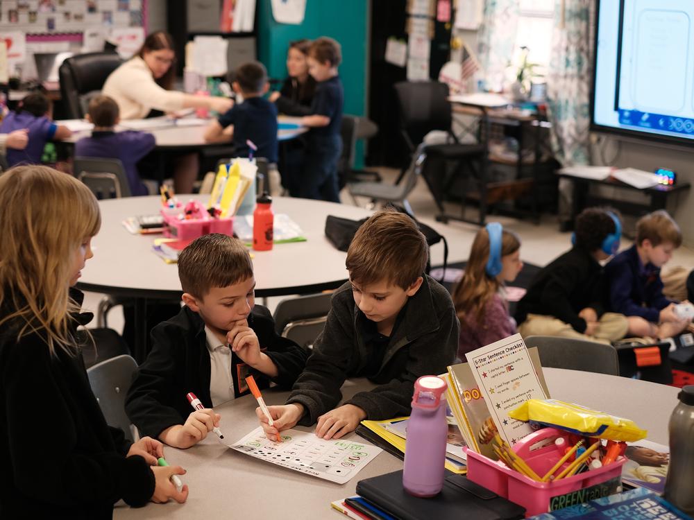 Second graders Serena Lacour, Luke Busby and Dylan Poche work on a word-identification reading game, while other groups work with their teacher, Cady Caskey, on sounding out words.