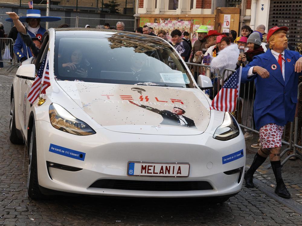 A reveler disguised as President Trump walks next to a car bearing a picture of Elon Musk's salute during the yearly carnival parade in the streets of Aalst, Belgium on March 2, 2025.