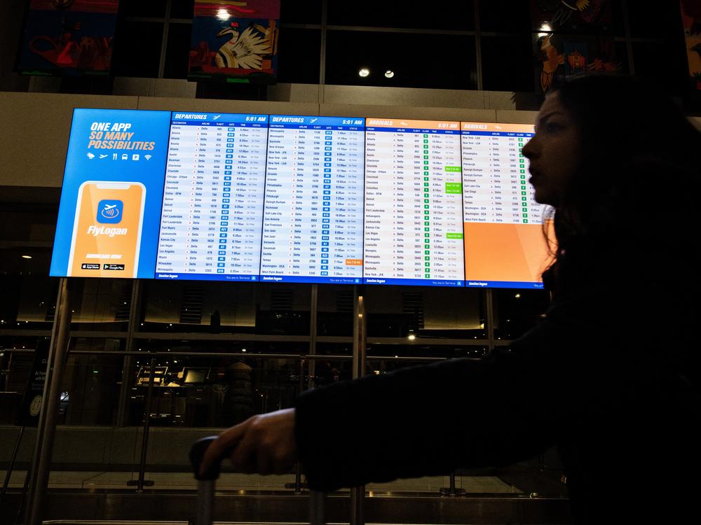 A person walks by an arrival and departure board at Boston's Logan Airport on Dec. 23, 2024.