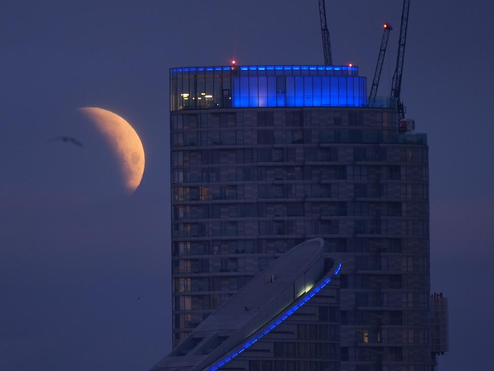A lunar eclipse is visible above Canary Wharf in London as the full moon passes into Earth's shadow.