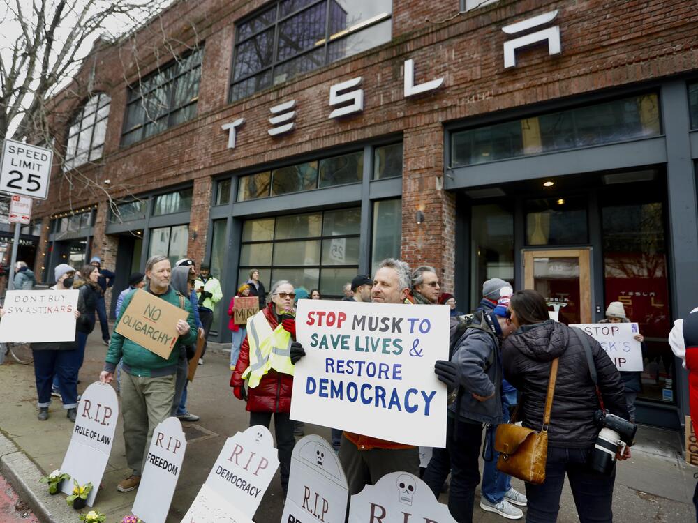 People protesting Musk's actions in the Trump administration hold signs outside a Tesla showroom in Seattle on Feb. 13