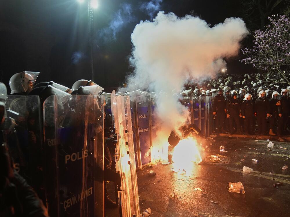 A protester holds a flare next to riot police officers during a protest against the arrest of Istanbul Mayor Ekrem Imamoglu, in Istanbul, Turkey, Saturday, March 22, 2025.