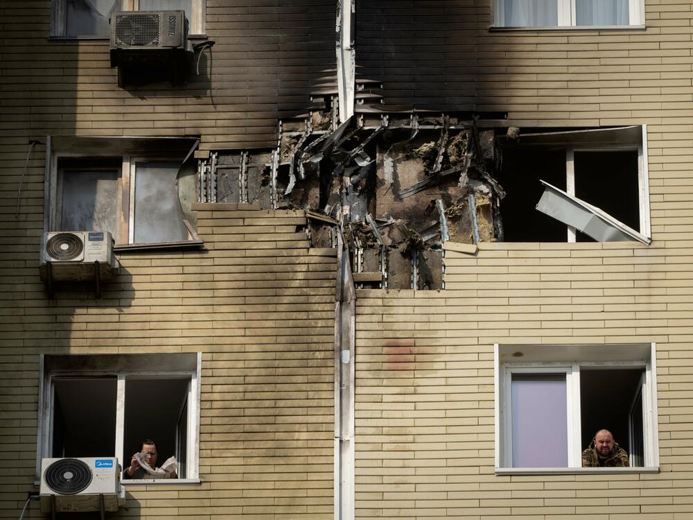 A resident watches as his neighbor cleans up a damaged apartment after a Russian drone attack in Kyiv, Ukraine, March 23.