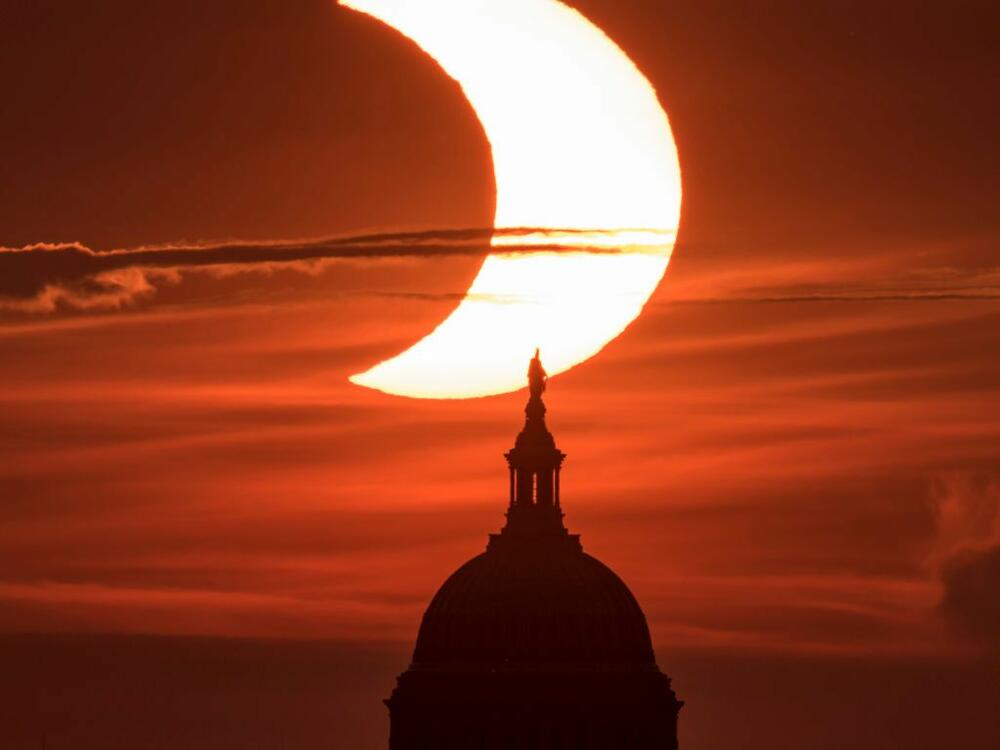 A partial solar eclipse is seen as the sun rises behind the U.S. Capitol building on June 10, 2021.