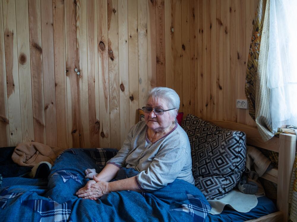 Neonila Prytsyk sits in her bed in a temporary housing unit in Posad-Pokrovske, on the land where her home stood before it was destroyed. 