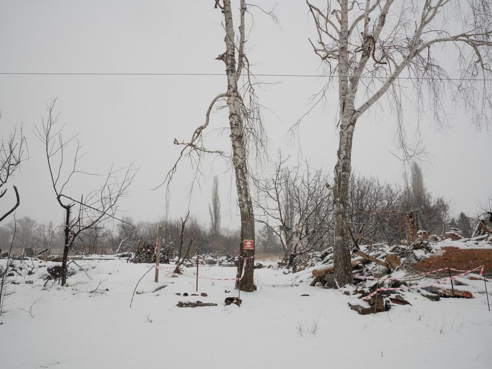 Destroyed homes in Staryi Saltiv are blanketed with snow in February. A sign warns of landmines and tape marks pieces of possibly unexploded ordnance on the ground.