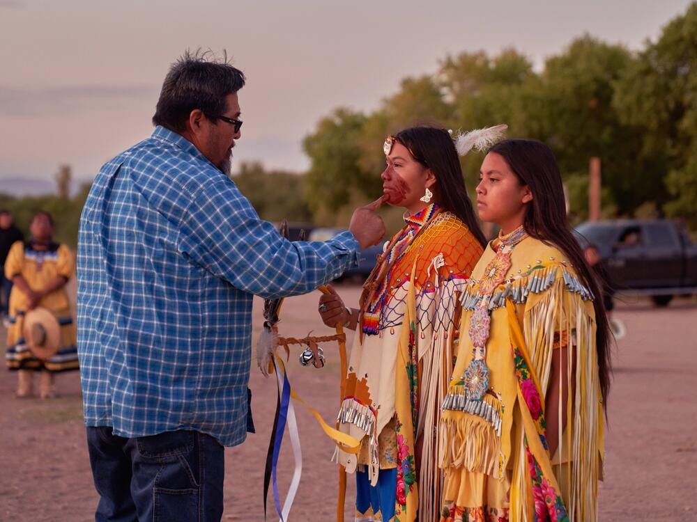 Medicine man Budd Cooley paints Ava Victoria Bryce Olquin's first attendant, Deanna Grey, at the Beaver Springs Dance Ground in San Carlos, Ariz.