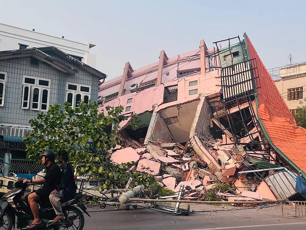 People drive on a motorbike past a collapsed building in Mandalay on March 28, 2025, after an earthquake in central Myanmar.