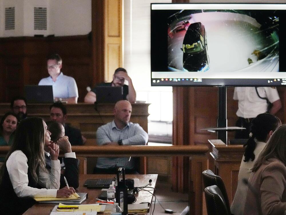 Karen Read, at left, watches as Massachusetts State Police Trooper Joseph Paul testifies about her vehicle, which is shown in on the video display, during her first trial in June 2024.