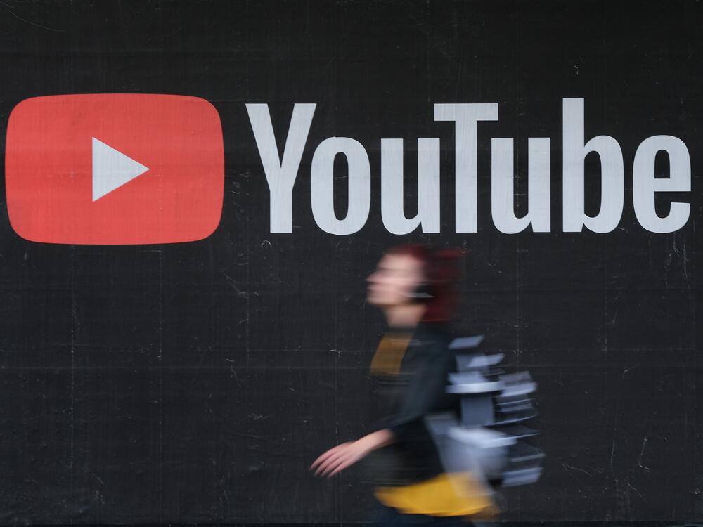 A young woman wearing headphones walks past a billboard advertisement for YouTube in 2019 in Berlin, Germany.
