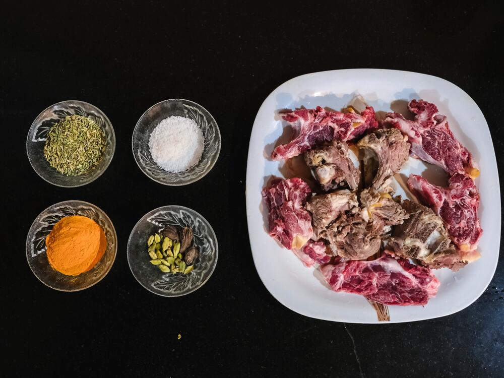 Left: A tray holds the key ingredients — goat meat, fennel seeds and mild spices. Simple and nourishing, these ingredients come together to make the comforting Kashmiri mutton soup. Right: Arsha Begum lifts a piece of tender goat meat from the golden broth — finally ready to eat. It's warm, nourishing and full of tradition, just as it has been for generations.