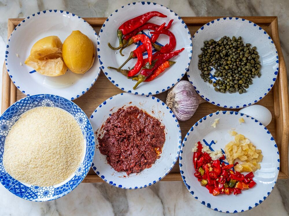 Ingredients for <em>hsou </em>are laid out on a platter. Top row, left to right: pickled lemons, pickled red peppers and capers; bottom row, left to right: semolina, harissa, diced pickled lemons and pickled peppers. 