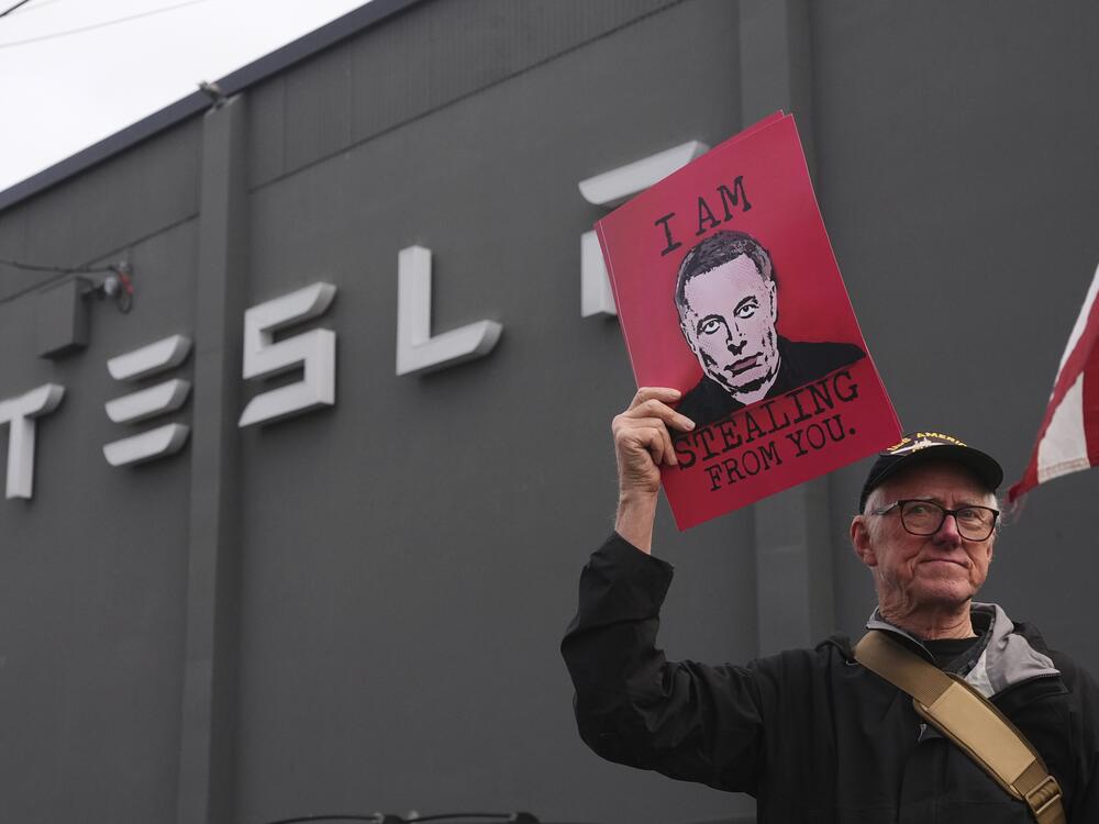 A man holds a sign depicting Elon Musk during a protest against Musk and Tesla on Saturday in Seattle.