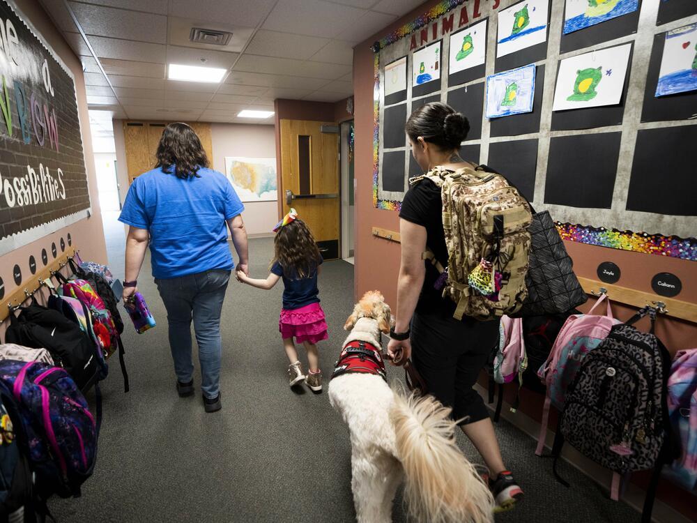 Special education teacher Vivien Henshall walks with student Scarlett Rasmussen, 8, as Scarlett's mother, Chelsea, follows with a service dog. Because of her disabilities, Scarlett needs regular access to a nurse at school.