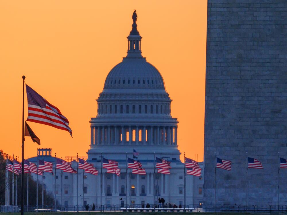 Sunrise turns the sky orange behind the U.S. Capitol building as it illuminates the U.S. flags circling the base of the Washington Monument on March 23 in Washington, D.C.