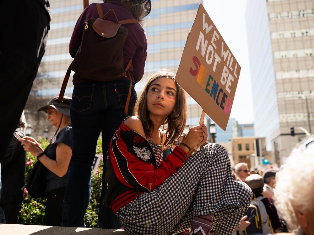 Juniper Tinker Ward waves a homemade sign during a protest against Elon Musk and Donald Trump in Oakland on April 5, 2025.