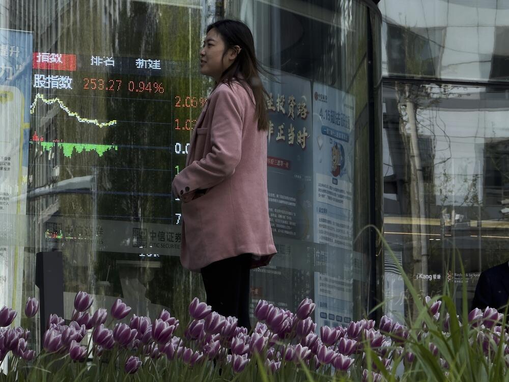 People stand outside a brokerage house, as an electronic board displays shares trading, in the Central Business District in Beijing on Thursday.