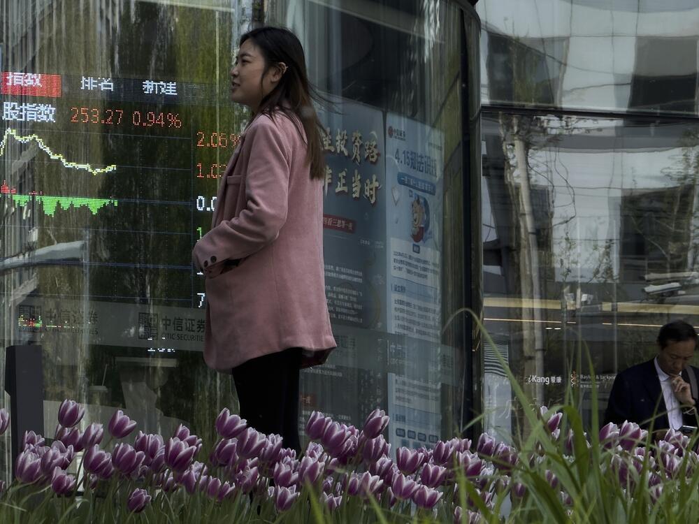 People stand outside a brokerage house as an electronic board displays shares trading index in the Central Business District, in Beijing on Thursday.