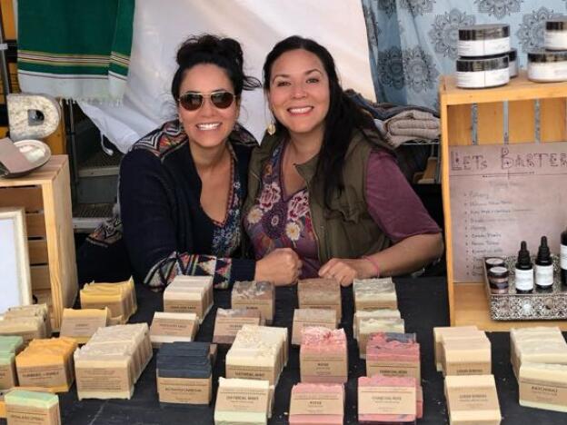 Cyndi Benitez (right) and her sister Christina Britts pose for a photo at their soap booth, Earth Soap Company, at the Okanogan Family Barter Faire. A sign to the right of Cyndi says 