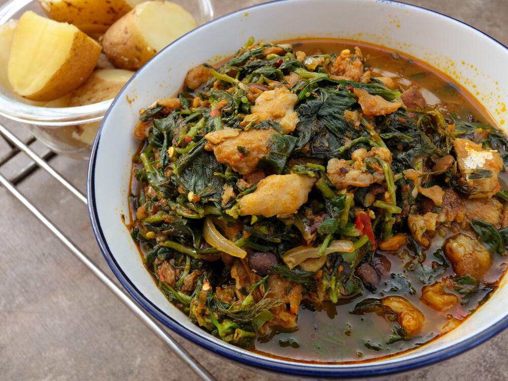 A bowl of freshly prepared waterleaf soup with a side of boiled potatoes.