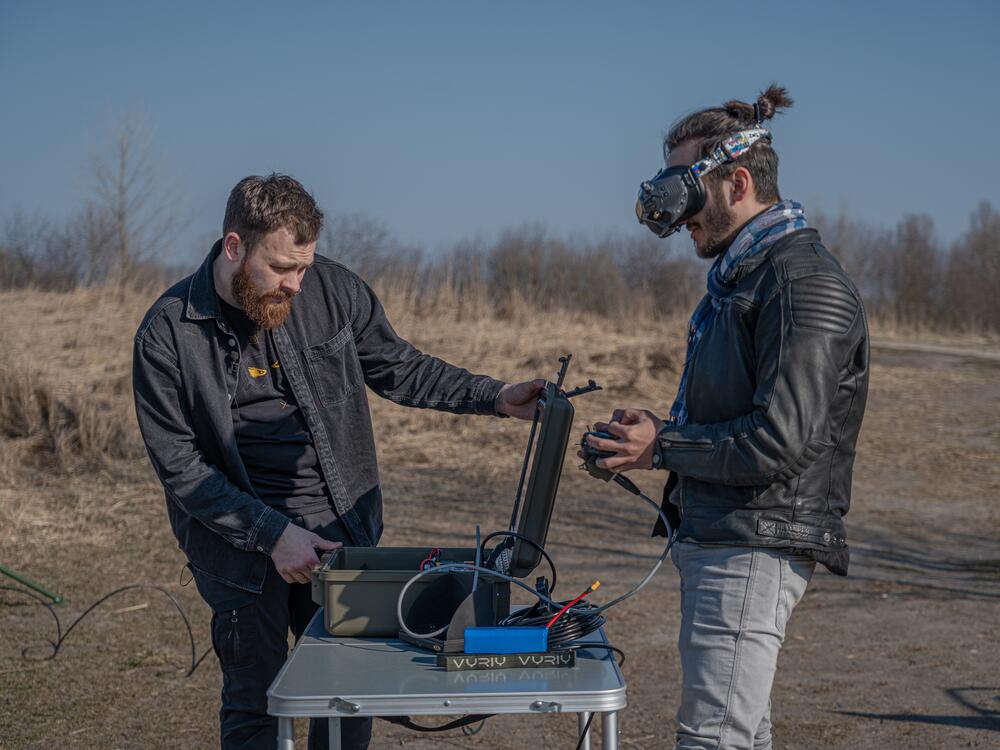 Vyriy CEO Oleksii Babenko (right), with a colleague, wears drone goggles to fly one of his drones in a practice field.