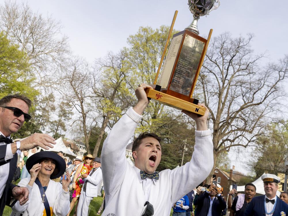 U.S. Naval Academy croquet team Imperial Wicket's Liam Wert holds a trophy above his head as he celebrates his team's win over St. John's College in the 2025 Annapolis Cup. At left is Annapolis' mayor, Gavin Buckley, and Superintendent of the U.S. Naval Academy, Vice Adm. Yvette M. Davids.