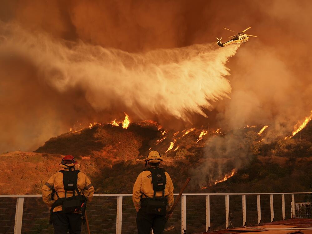 Firefighters watch a helicopter drop water on the Palisades Fire in Mandeville Canyon in Los Angeles in January 2025. California sued oil and gas companies in 2023 for allegedly misleading the public about the dangers of fossil fuels, which are the primary cause of climate change. The fossil fuel industry says lawsuits like California's are meritless and politicized.