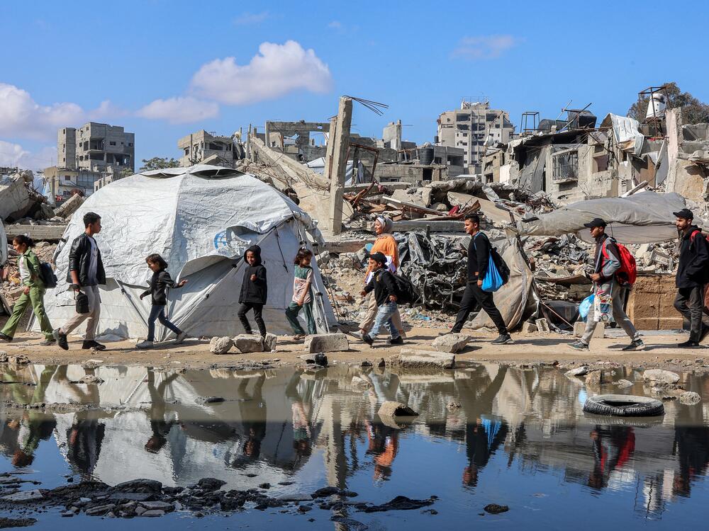 People walk by a tent shelter near the rubble of a collapsed building in western Gaza City on April 15.