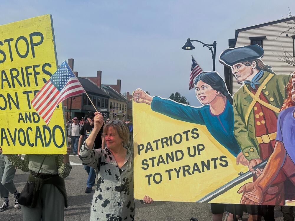 Protesters hold signs during a parade honoring the 250th anniversary of the American Revolution on Saturday in Concord, Mass.