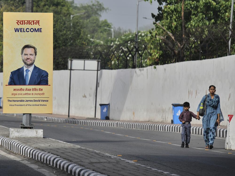 A woman and a child walk past a banner welcoming U.S. Vice President JD Vance on a street in New Delhi, India, on Monday.