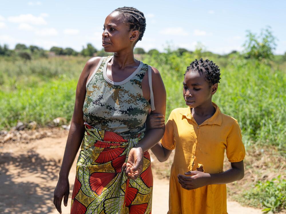 Theresa Mwanza and her daughter, Dorcas, stand in a field near their house. After their USAID-funded clinic closed, Theresa tried to get HIV medications at a government-run clinic but was turned away and told she needed to get 