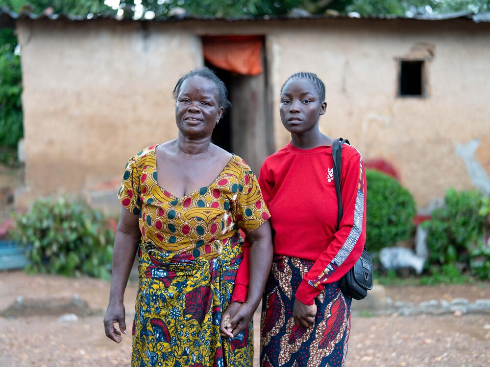 Catherine and her grandmother hold hands outside their home.