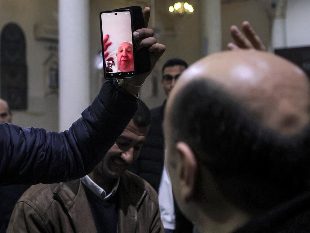 A man holds up a phone for the Rev. Gabriel Romanelli, parish priest of Gaza City's Roman Catholic Church of the Holy Family, to have a video call with Pope Francis as the pope blesses the congregation during Christmas Eve Mass, Dec. 24, 2024.