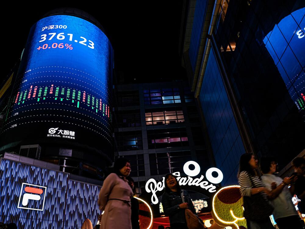 People walk past a screen showing the CSI 300 Index at a shopping mall in Guangzhou, in southern China's Guangdong province.