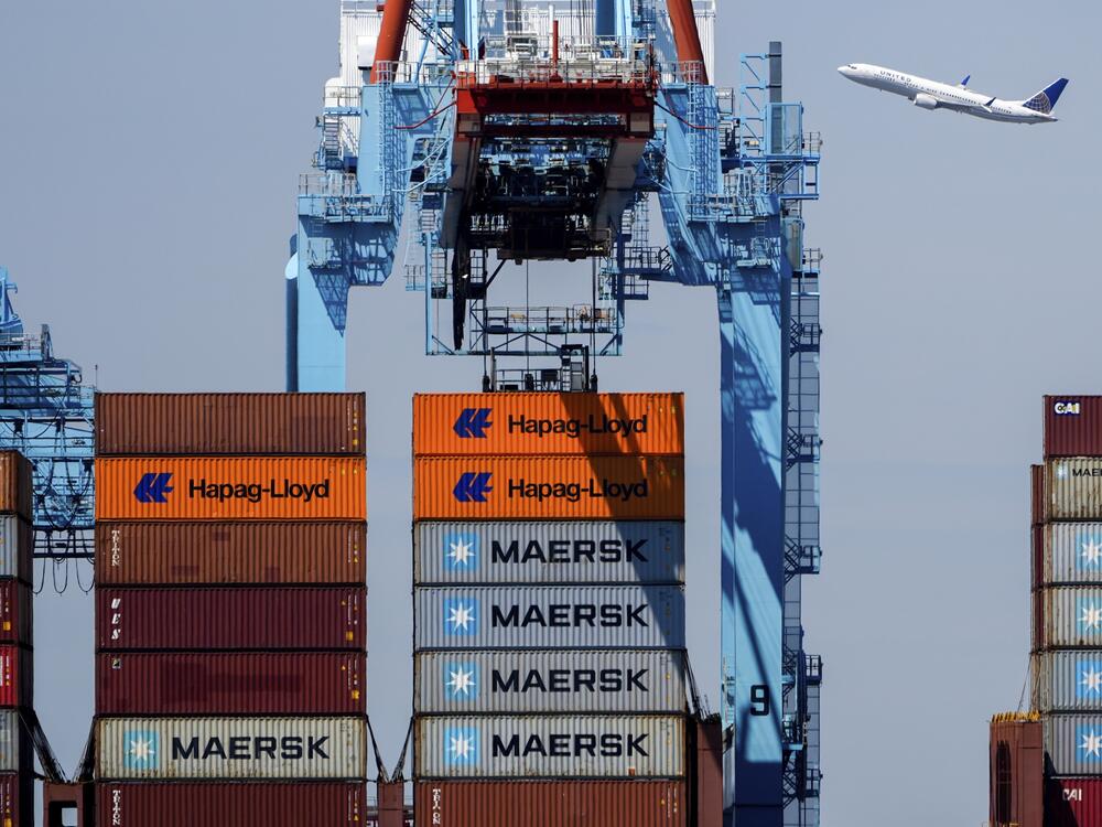 An airplane flies over the container ship Alexandra at the Port Newark Container Terminal on April 18 in Newark, N.J.