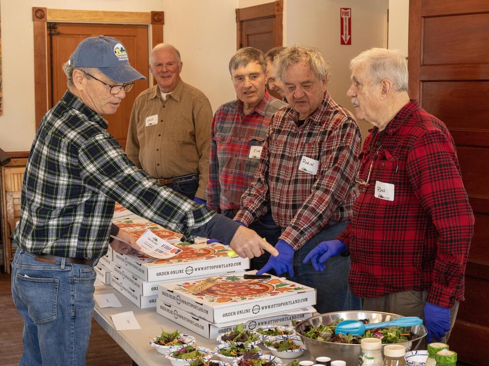 Attendance has more than quadrupled since the free ROMEO lunches for older men started in Harpswell, Maine, last fall. Tom Mahoney, left, directs other volunteers at a recent lunch when pizza was on the menu.